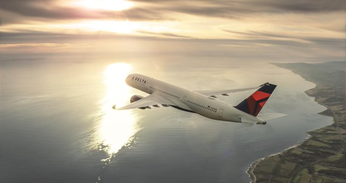 A white, blue and red plane flying over the ocean at sunset