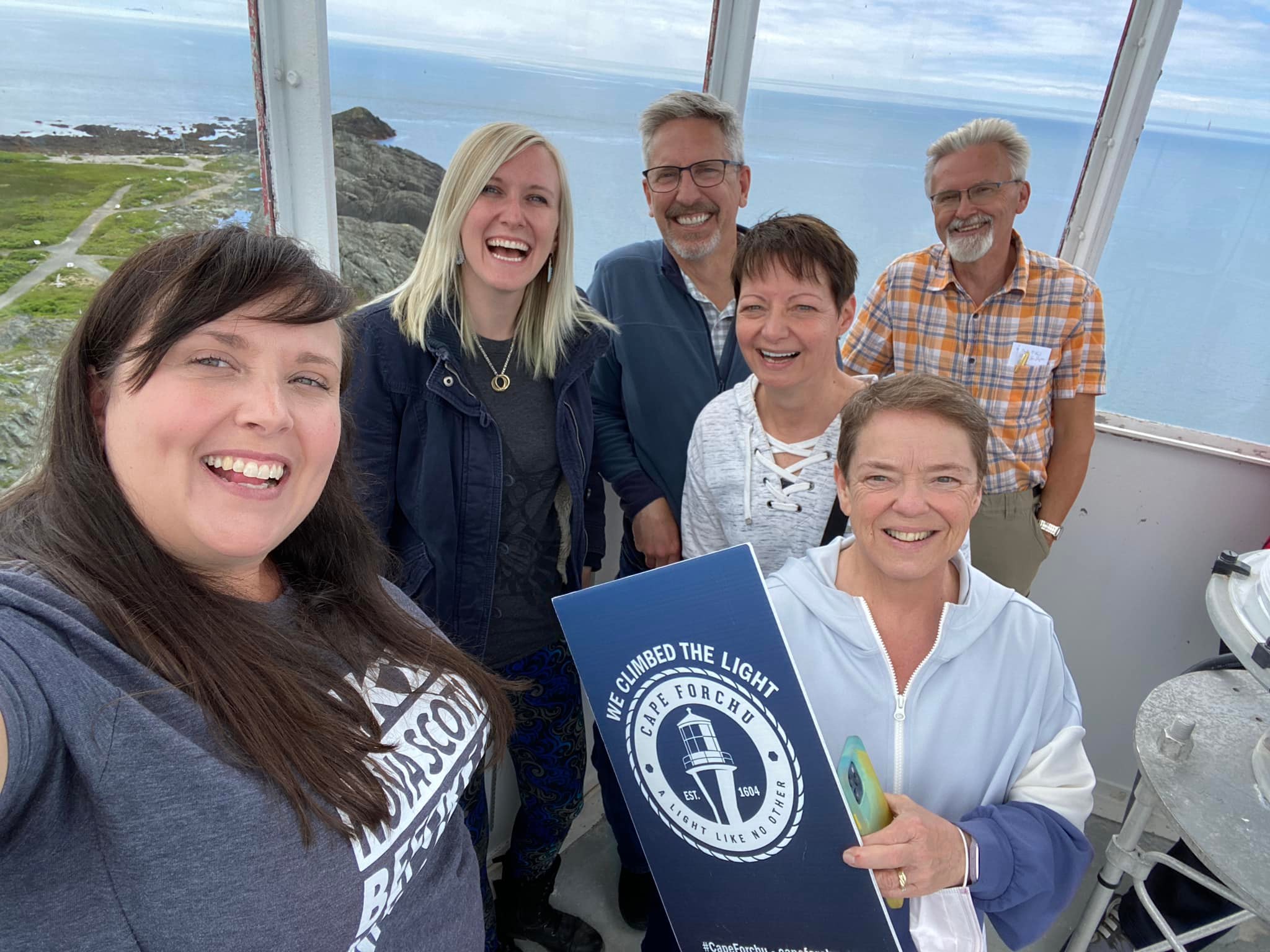 Group of people standing in the top of Cape Forchu Lighthouse with a sign that says I climbed the light.