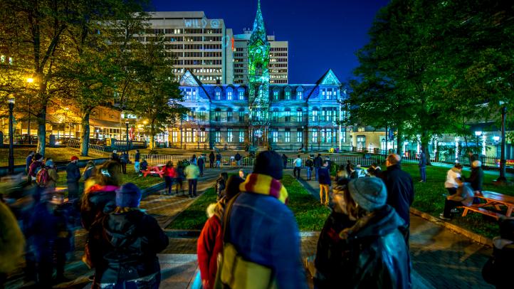 People in groups in front of Halifax Grand Parade watching a lightshow.