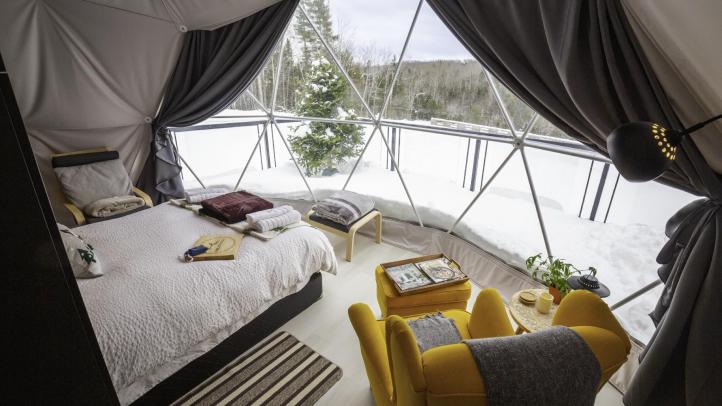 Inside view of camping dome at Valley Sky Luxury Camping. A bed and yellow arm chair face a window looking out at the Annapolis Valley in winter.