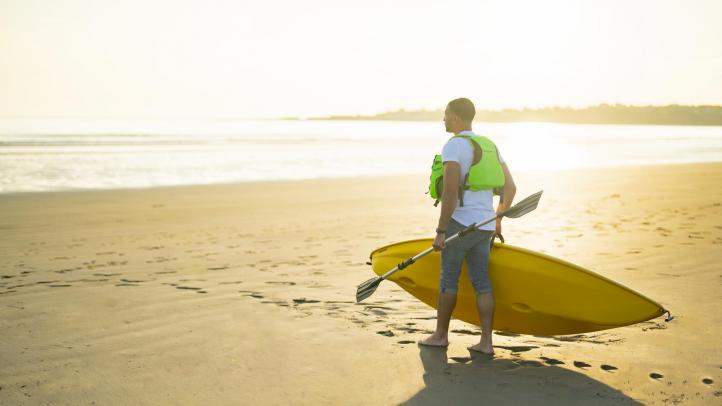 A man in a life vest carrying a kayak toward the shore at Mavillette Beach Provincial Park