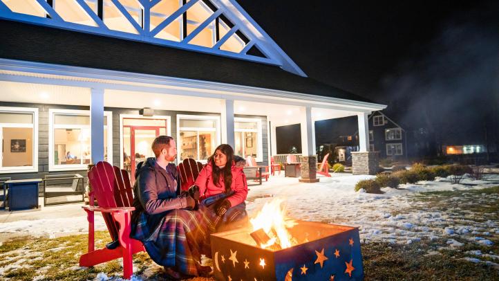 Two people sitting outside a night by a fire in the snow