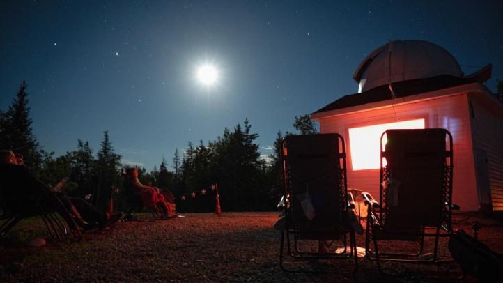 Two people in lawn chairs sitting outside at night under the moon