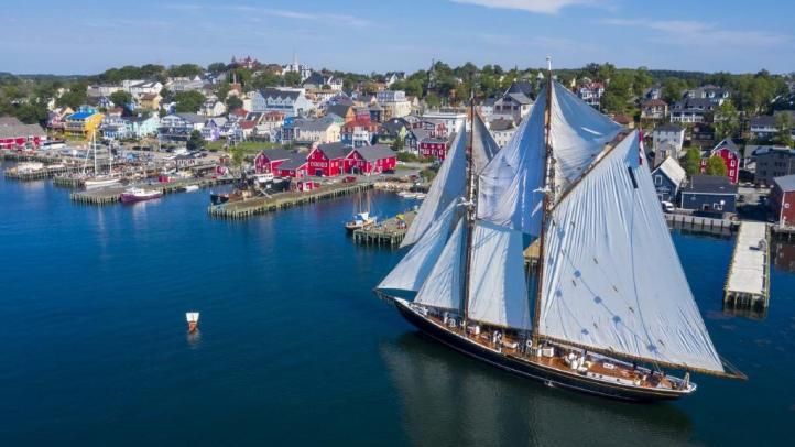 A drone captures the Bluenose II sailing ship coming in to the dock on the Lunenburg waterfront. The ships sails are full and the weather is sunny. 